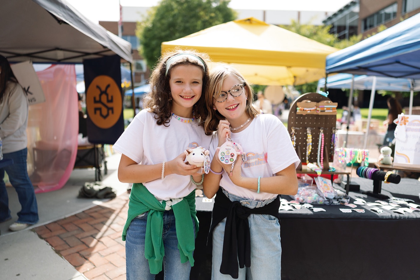 Two kids holding handmade goods in front of a bracelet display