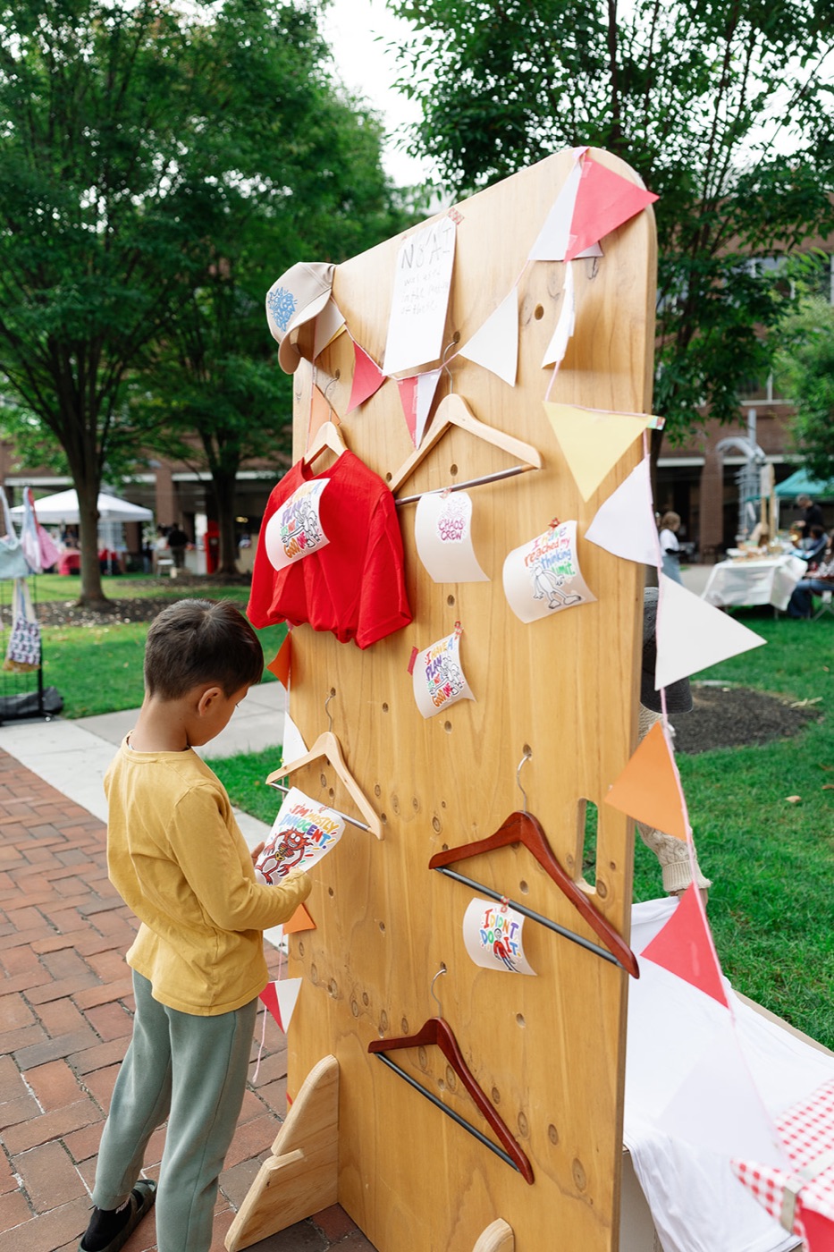 A kid looking at hand-painted shirts hung on a wooden pegboard