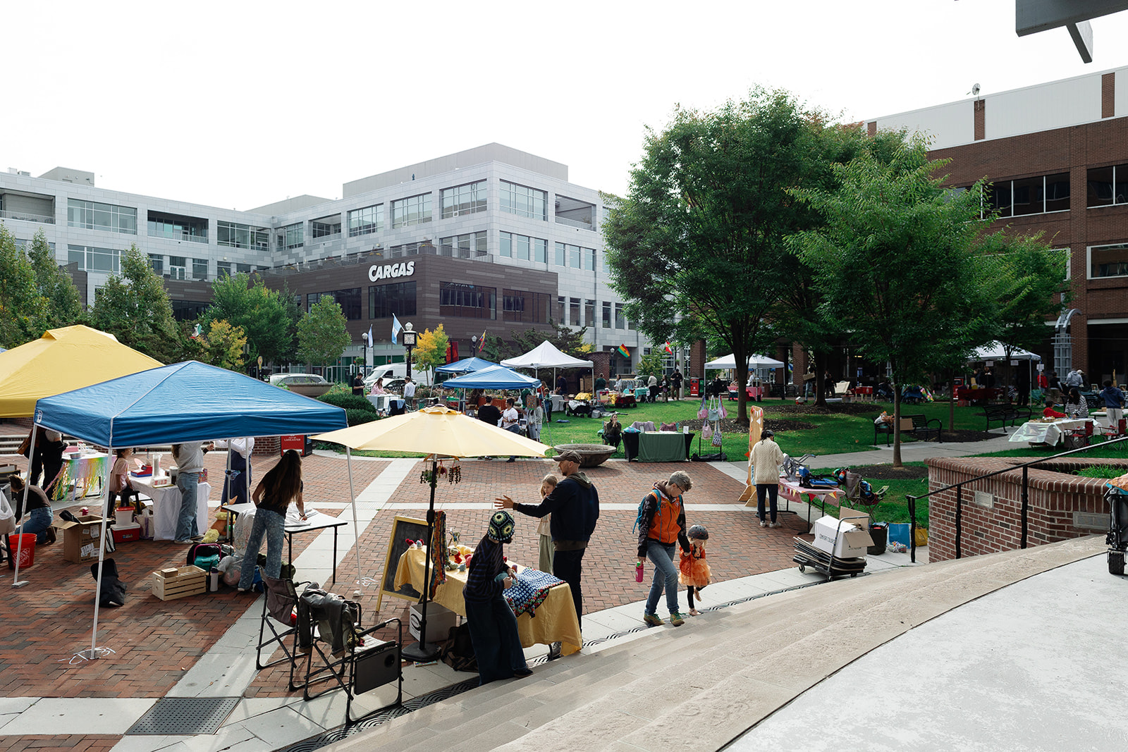 Kid-run booths under yellow and blue canopies across Binns Park, with shoppers walking between them